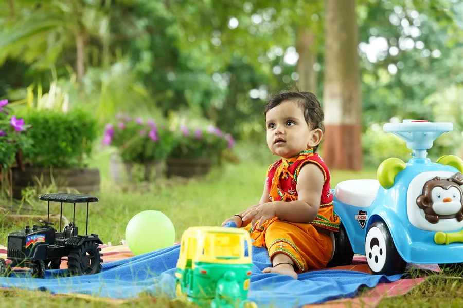 Baby sitting up on a blanket in the garden, toys spread out around him