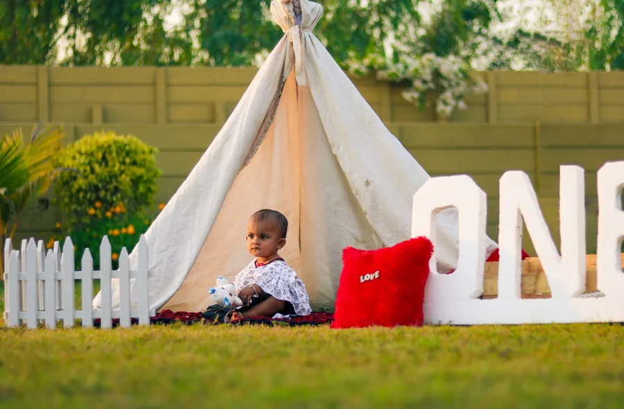 One-year-old in a garden tent setup beside the ONE letters at a first birthday shoot