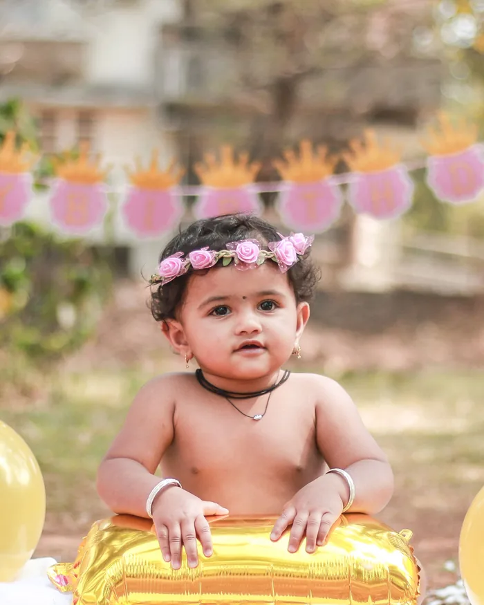 Baby holding a gold balloon at an outdoor first birthday setup
