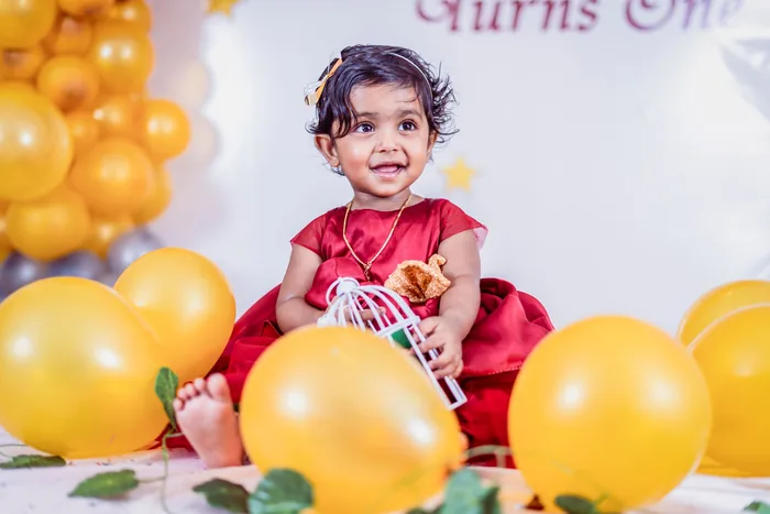 One-year-old in a red dress among balloons at her first birthday setup