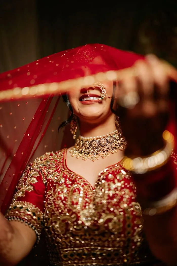 Bride laughing as she lifts her dupatta, in full gold jewellery