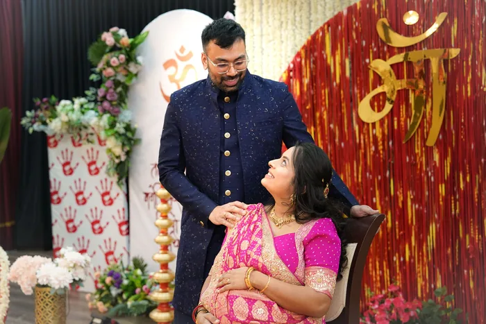 Expectant parents together at the godh bharai backdrop, a lamp lit beside them