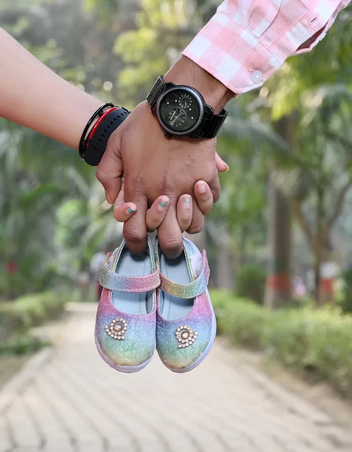 Parents holding a pair of baby shoes between them, outdoors