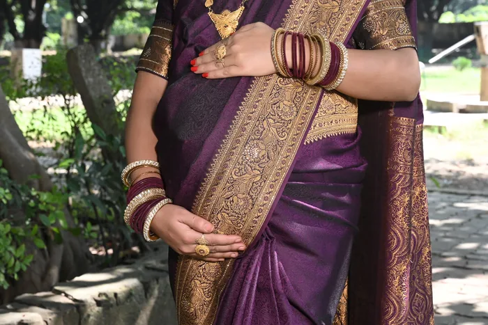 Expectant mother in a purple and gold silk saree, her hands resting on the bump