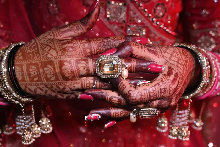 The bride's mehndi hands resting on her red lehenga, rings and bangles close in
