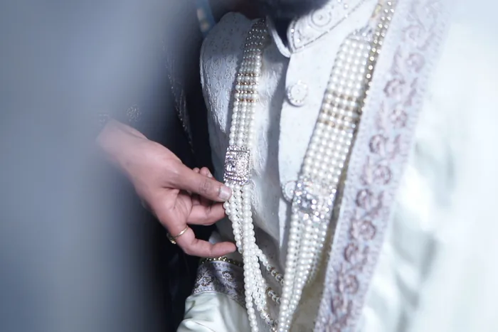 Hand adjusting the pearl mala on the groom's white sherwani